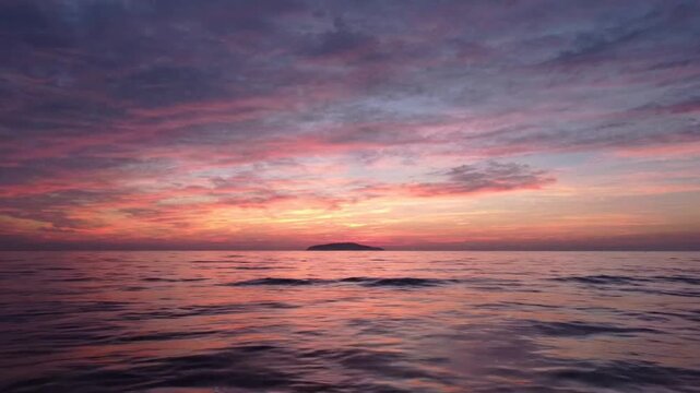 Ocean sunset with distant island silhouette at twilight, serene tropical seascape background horizon