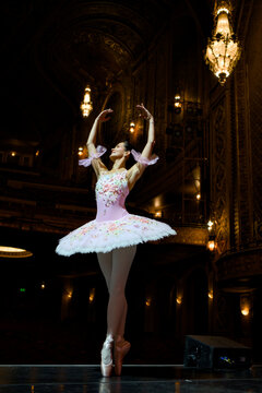 Ballerina in pink tutu posing beneath theater chandeliers