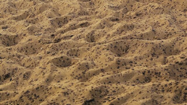 Slow motion of first raindrops impacting dry sand on a summer day, creating small craters and dark spots on the ground, representing the beginning of a storm or the concept of thirst and relief