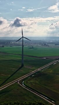 Single wind turbine rotates above green farmland near Schwedt Germany under cloudy sky with long shadow stretching across fields