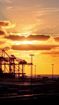 Port container cranes stand beneath glowing sunset clouds in Bremerhaven, Germany, vertical backdrop with pallet trolleys in aisles