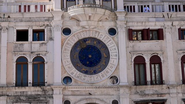 St Mark's Clocktower zodiac dial fills the frame against the worn marble facade and surrounding windows in Piazza San Marco.
