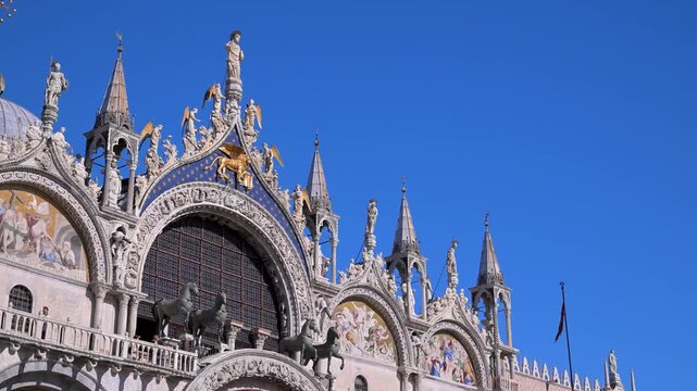 Facade of St Mark's Basilica with bronze horses, statues, and mosaics framed against a deep blue sky in Venice.