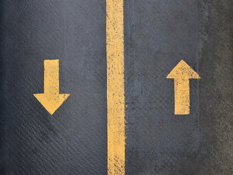 two yellow arrow pointing in opposite direction with dividing line on black asphalt background