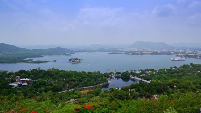 Lake Pichola and Jag Mandir overlook a foreground of trees, red blossoms and the smaller Doodh Talai waterbody in Udaipur.