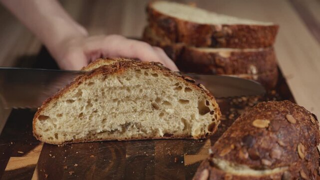 Close-up of hands slicing freshly baked artisan sourdough bread with a knife on a wooden cutting board. Homemade crusty open crumb loaf for breakfast, bakery promos, and healthy food concepts.