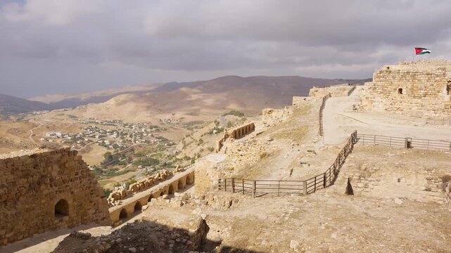 4k Handheld panning view, medieval Kerak Castle ruins above Al-Karak, Jordan, showing stone fortifications, the Jordanian flag and surrounding arid mountain valley