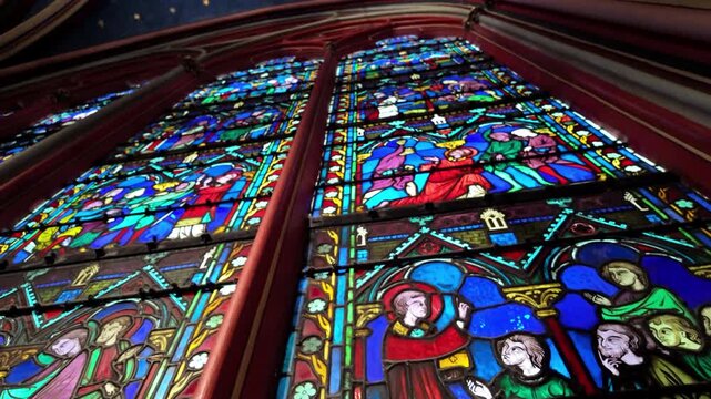 Colorful stained glass panels in Sainte-Chapelle rise toward a starry vaulted ceiling as the camera tilts upward.