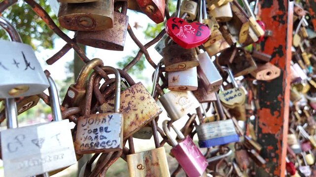 Red heart-shaped Paris love lock hangs on a crowded fence of padlocks as the camera glides along the row.
