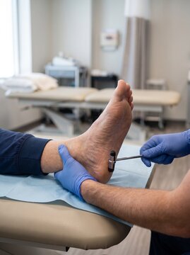 Doctor examining patient foot with reflex hammer in medical clinic