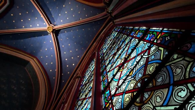 Colorful stained glass windows rise toward a deep blue vaulted ceiling with gold stars inside Sainte-Chapelle.