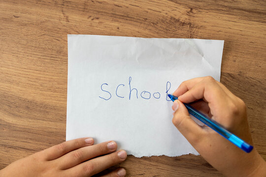 Writing the word school on paper with a blue pen