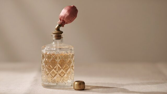 Vintage glass perfume bottle with pink atomizer and gold cap on neutral background