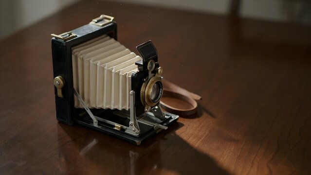 Vintage folding bellows camera placed on wooden surface with shadow detail