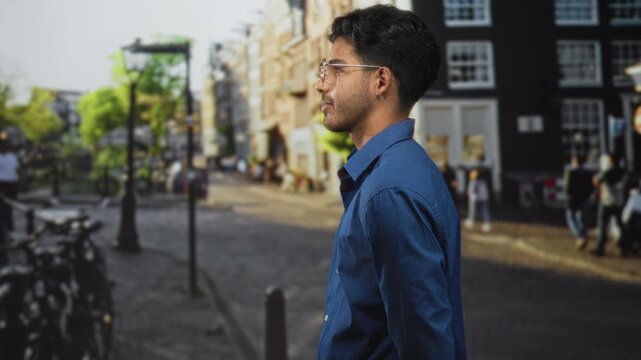 Young hispanic man wearing glasses and a blue shirt looks to the side showing his face on a city street; contemplation.