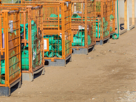 Green PVC pipe fittings stored in orange metal gitterbox crates at an outdoor civil engineering site, showcasing industrial logistics, infrastructure materials, construction supply.