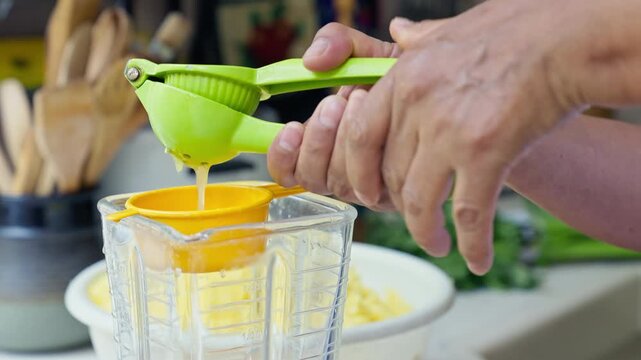 Hands squeezing fresh lime juice using a green manual press into a blender