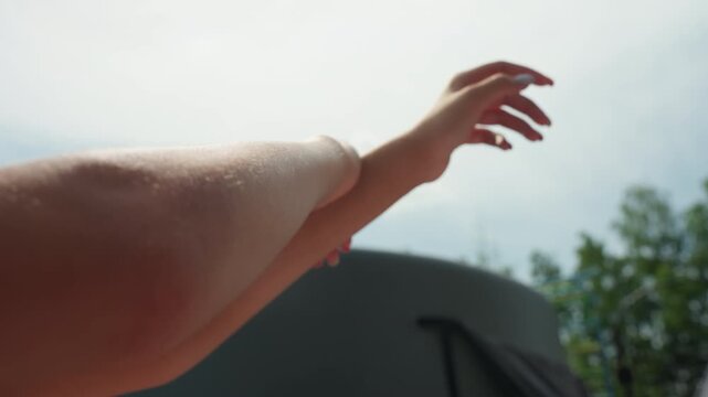 Woman arm and hand showing skin texture details as woman raises her limb against outdoor background with trees and sky. focus remains on smooth surface from various angles emphasizing