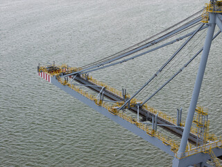 Large Metal Crane Boom Extending Over the Water at a Busy Cargo Port During the Bright Daytime Hours © Tom
