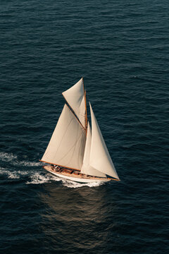 Sailboat gliding over the ocean with white sails and blue water under clear skies at a sunny time of day