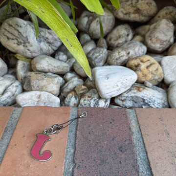 Magenta letter J keychain on a brick ledge with pebbles