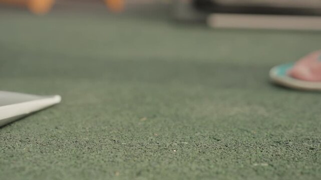 Close up view of green textured floor with occasional foot movements and objects like flip flops and tubes appearing. scene focuses on ground level details showing subtle changes