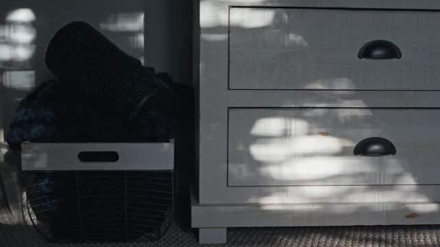 Sunlight and leaf shadows move across a white wooden dresser