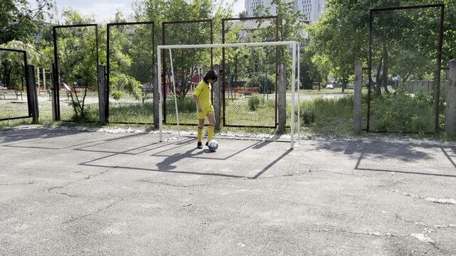 Teen football player practicing offensive play dribbling ball and shooting at goal on outdoor court youth sport training concept. High quality FullHD footage