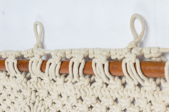 Close up of handmade macrame curtain featuring natural cotton rope knots attached to a wooden rod with hanging loops showcasing boho textile craft woven decor artisan design and home decoration.