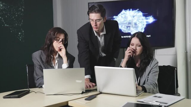 Three professionals in a business meeting setting with laptops, focused on a screen showing an AI-themed digital brain graphic and code.