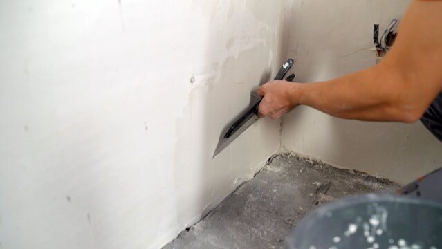 Worker's hand applying plaster to a drywall corner with a wide putty knife, smoothing the surface during home renovation or construction