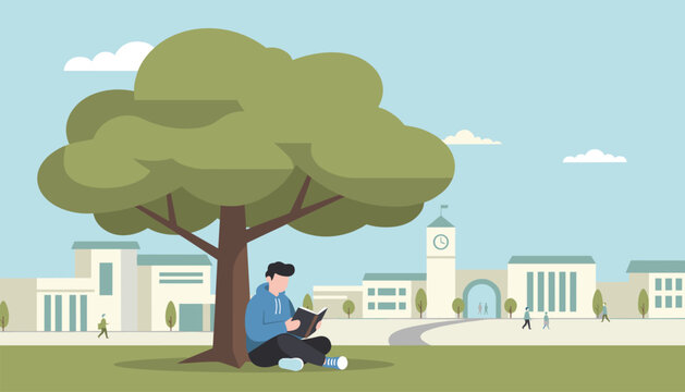 Young male student sitting cross legged and reading a book under a large shady green tree on a university campus lawn.