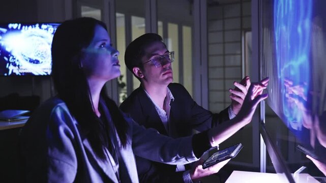A professional man interacts with a high-tech circular data interface on a large digital screen, featuring graphs and data elements in a glowing blue theme.