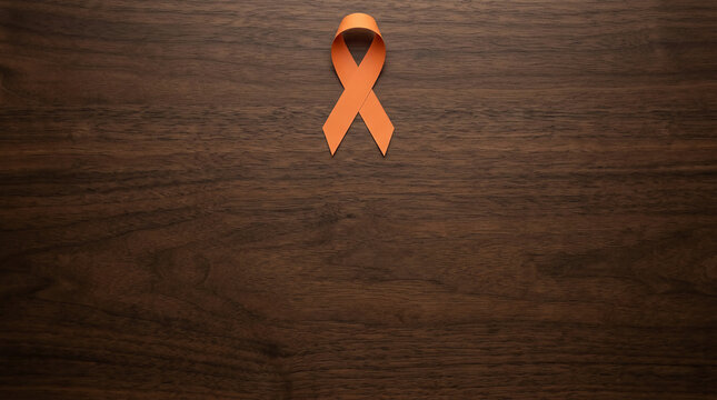 An orange awareness ribbon symbol rests on a dark textured wood background, representing leukemia and kidney cancer awareness with professional lighting and minimalist flat lay style.