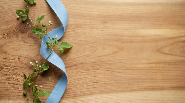 Blue linen ribbon entwined with green botanical vine resting on rustic oak wood surface, soft natural lighting, minimalist aesthetic flat lay with copy space for greeting card design.