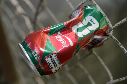 crushed aluminum Coca-Cola can with international soccer tournament branding stuffed into a barrier mesh fence in Toronto