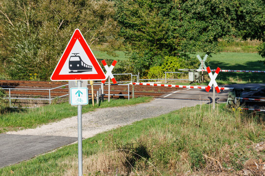 klassischer Bahn&uuml;bergang auf dem Land an Fahrradweg mit geschlossener Schranke und mit Hinweisschild