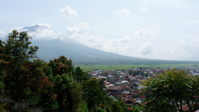 Beautiful view of Mount Kerinci surrounded by clouds, featuring stretches of rice fields and rural atmosphere