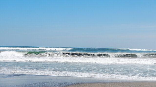 Scenic view of ocean waves rolling onto a sandy beach under clear blue sky