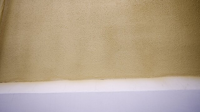 Beige popcorn texture ceiling detail against white painted wall with small cracks, minimalist architectural background