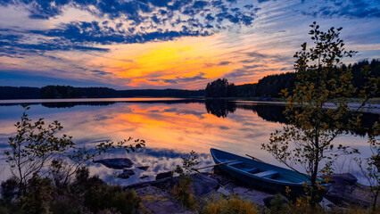 Scenic view of wooden boat on calm lake water with vibrant sky reflection Finland © Light&Lens