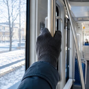 Gloved passenger hand holding a metal rail inside public transport during winter travel