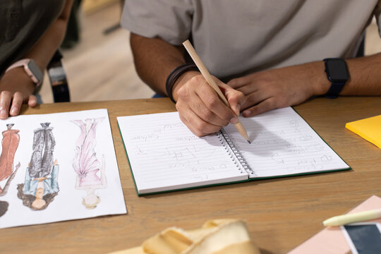 African American designers sketching on spiral notebook with pencil and swatches at wooden table