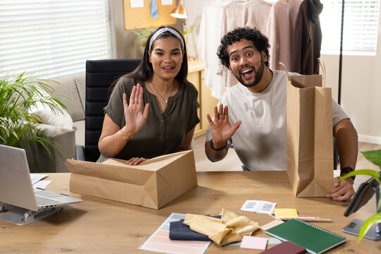 African American business partners waving, packing parcels in home studio with laptop and kraft box