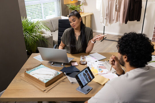 African American woman sitting at laptop wearing olive top using phone reviewing swatches in studio