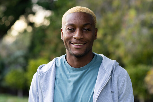 African American man standing outdoors smiling, wearing gray zip hoodie, teal tee