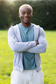 African male standing with arms crossed in grassy field wearing gray zip hoodie and teal t-shirt