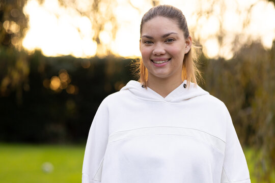 Adult African American woman standing on park grass, smiling, wearing white hoodie