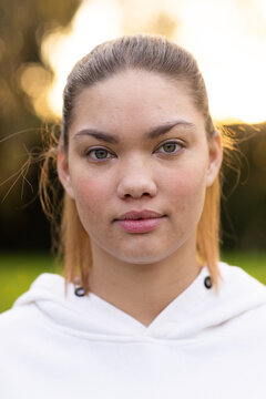 African American woman gazing at camera at park wearing white hooded sweatshirt with black grommets