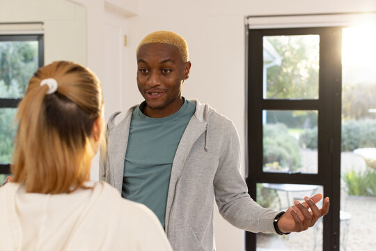African American friends chatting, man gesturing with both hands, woman listening by glass door